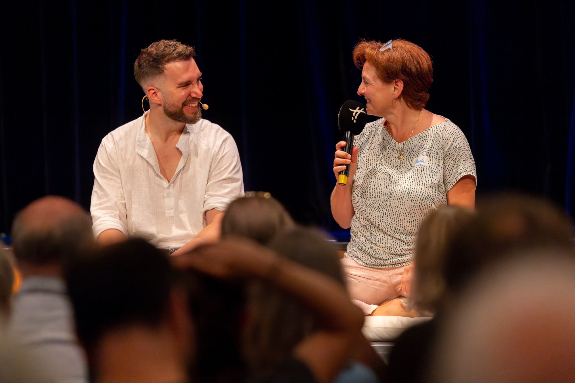 Alexander Hartmann und eine Teilnehmerin lachen im persönlichen Gespräch auf der Bühne